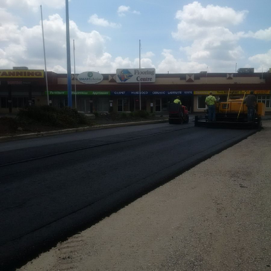 A road with some workers laying asphalt on it